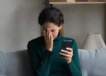 Woman looking stressed while using a phone, highlighting the dangers of social media during bankruptcy